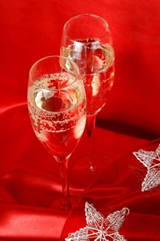 Close-up of two glasses of champagne and some Christmas decorations over a red fabric background