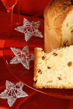 Panettone the italian Christmas fruit cake served on a red glass plate over a red background with silver star shaped decorations. Selective focus.