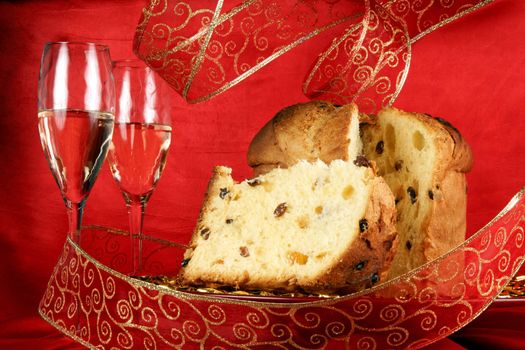 Panettone the italian Christmas fruit cake served on a red glass plate over a red background with golden star decorations, ribbon and two glasses of champagne. Selective focus.