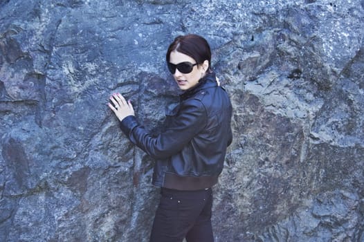 Attractive woman in sunglasses posing near the rock