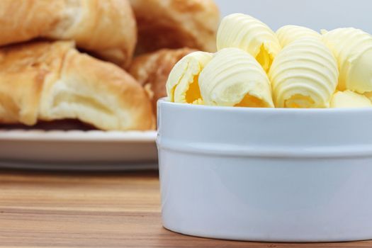 Curled butter in a dish with croissants in the background.