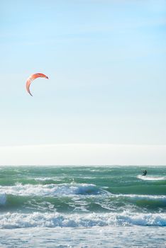 Surfer with red kite surfing off the beach in San Francisco, California on a sunny day.