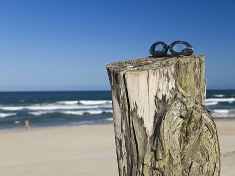 A pair of goggles sitting over a log in the beach.