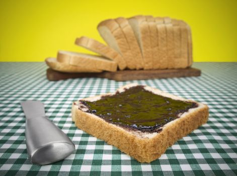 A slice of bread spread with jam. Loaf of bread on the background.