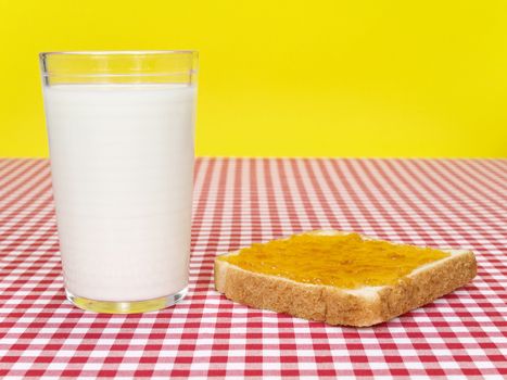 A glass of milk and a toast spread with jam over the table.