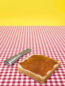 A slice of bread spread with jam and a knife over the table.