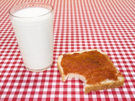 A glass of milk and a toast spread with jam, with a bite missing.