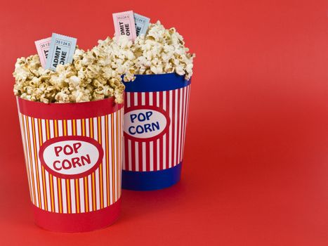 Two popcorn buckets over a red background. Movie stubs sitting over the popcorn.