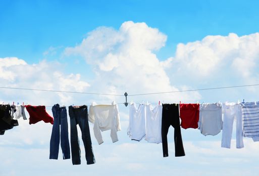 Pants and shirts on clothesline against beautiful white puffy cloud on a sunny day.