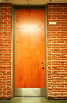 Office building or school wood door in olive green metal frame in terra cotta brick wall.