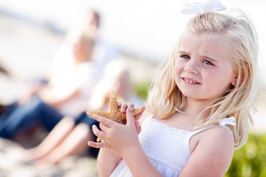 Adorable Little Blonde Girl with Starfish at The Beach.
