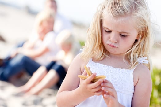 Adorable Little Blonde Girl with Starfish at The Beach.
