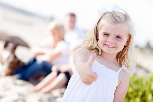 Adorable Little Blonde Girl with Thumbs Up At the Beach with Her Family.