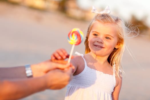 Adorable Little Girl Picking out Lollipop from Mom at the Beach.