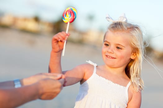 Adorable Little Girl Picking out Lollipop from Mom at the Beach.