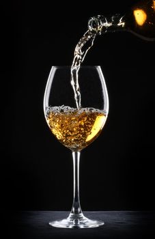 Pouring white wine into a glass over black background