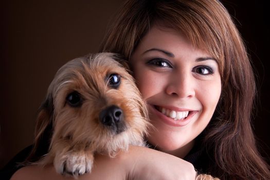 A young woman in her 20s holds a cute mixed breed beagle yorkshire terrier dog.