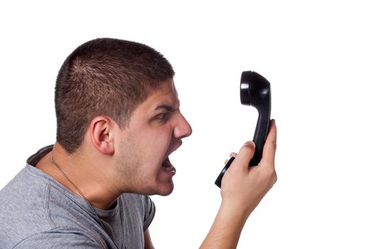 An angry and irritated young man screams into the telephone receiver over a white background.