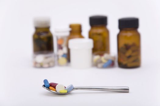 differently colored pills in spoon with other pills on the background