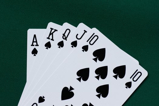 Playing cards - poker royal flush spades on green background.