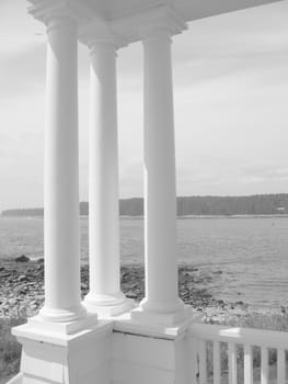 Three 19th century architectural columns at the ocean's edge, in black and white