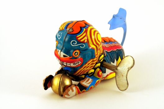 Wind-up toy dragon from China with blue tail and a golden ball in its paws, made of brightly-painted metal.  The winding key is visible in its side.

