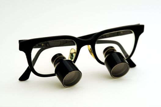 A pair of magnifying glasses for surgical use with the earpieces folded closed.