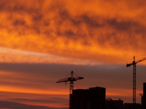 Sunset. Bright clouds. Two lifting cranes. Building. 