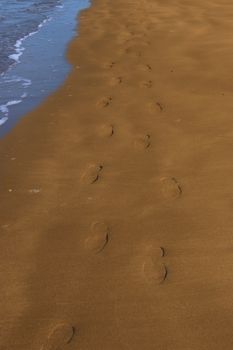 footprints left in the sand of an irish beach with the tide coming in