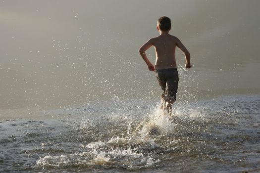 Young boy running in the shallow water of a river