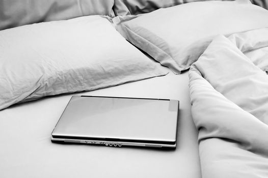 Black and white image of a laptop on unmade bed