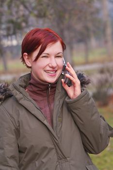 Smiling redheaded girl using a mobile phone in a park.Shot with Canon 70-200mm f/2.8L IS USM