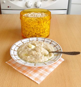 plate with porridge  and cupping-glass with oats flakes on a table on kitchen background