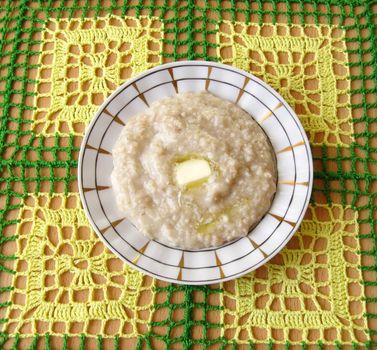 plate with porridge and slice of butter on a table covered knitted tablecloth