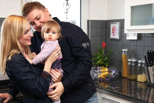 Young family home with a child. The family is in the kitchen and smiles,  mother carries the baby.
