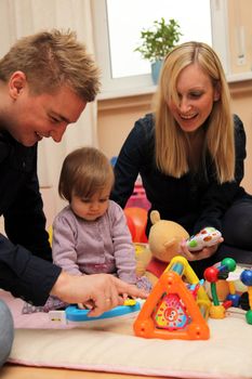 Mother and father happily playing with your child. The family is sitting on the floor with toys
  