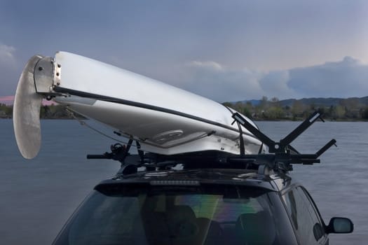 white kayak with aluminum rudder on car roof racks with a lake and mountains in background