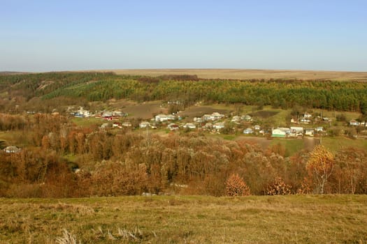 Fall rural landscape. The village in the valley among fields, forests and meadows