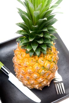 ripe vivid pineapple on a black plate with knife and fork