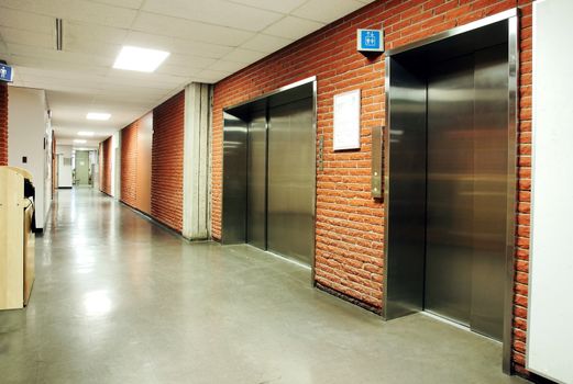 Freight and regular steel door elevators with signs in an empty hallway of modern building. Can be office, school, hospital.