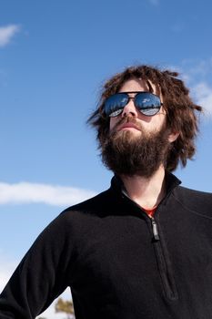 A male with a full beard and retro sunglasses standing in a winter landscape ready for adventure