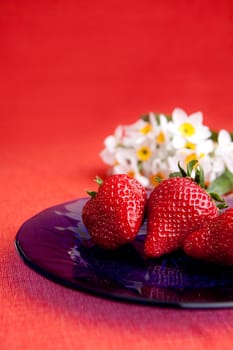 A plate of strawberries on a red table cloth