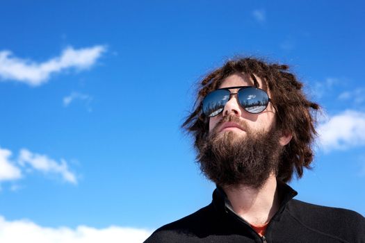 A male with a full beard and retro sunglasses standing in a winter landscape ready for adventure