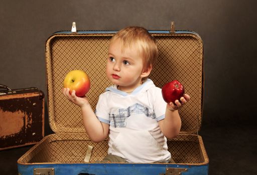 The little boy with a apples sits in a old suitcase
