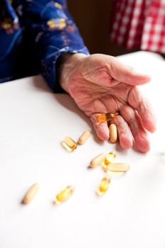 An old hand holding pills on a table