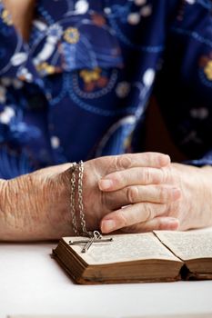 An old pair of hands with a book and cross - shallow depth of field with focus on cross