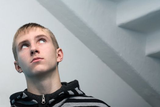 Looking up young guy standing on gray background with staircase. No glamour, natural