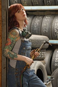 Photo of a young beautiful redhead mechanic wearing overalls and holding a welding torch.  Attached property release is for arm tattoos.
