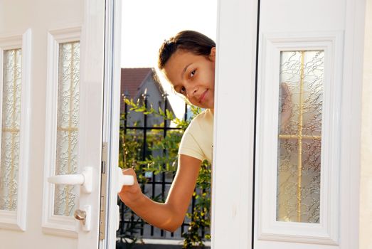 cheerful smiling caucasian teenage girl behind opened white front door looking inside