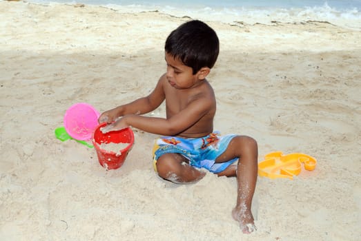 An handsome Indian kid playing with sand at a tropical beach